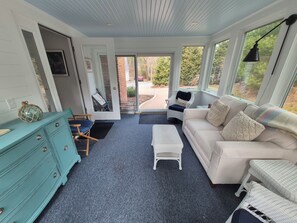 Ein Zimmer mit einem weißen Sofa, einer türkisblauen Kommode, einem Korbstuhl und einem kleinen weißen Tisch.