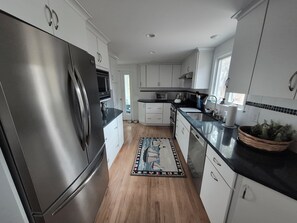 A modern kitchen with stainless steel appliances, white cabinetry, and a patterned rug. - Charming Coastal Cottage near Cockle Cove Beach (S. Chatham)
