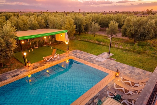 Piscina con sillas de descanso y un área de estar techada, rodeada de vegetación.