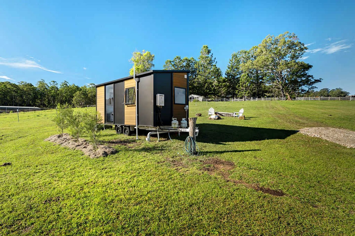A small, single-story mobile home with a flat roof, situated on a grassy field with trees in the background.