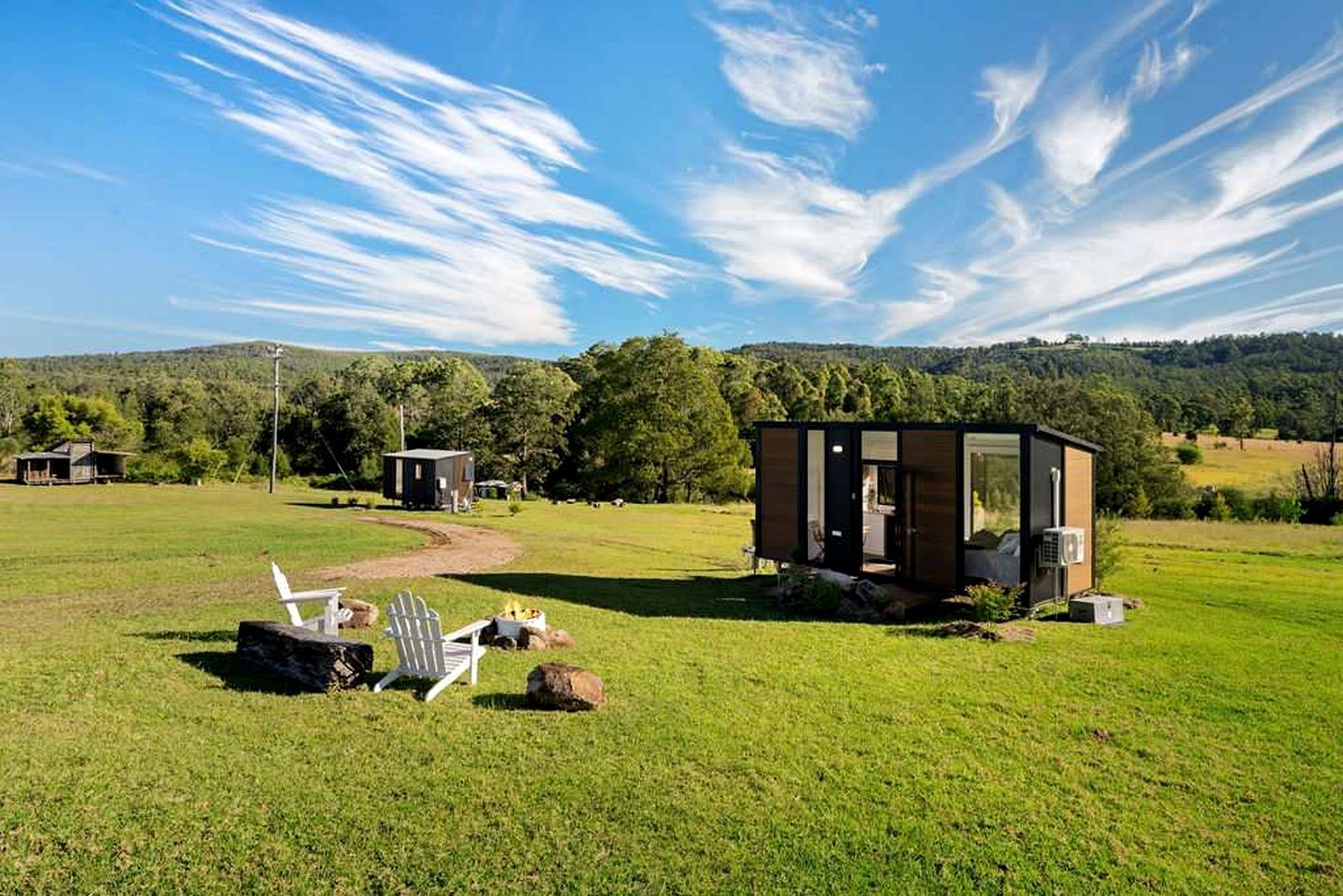 A modern outdoor structure with a glass door, surrounded by a grassy field and trees, with a clear sky above.