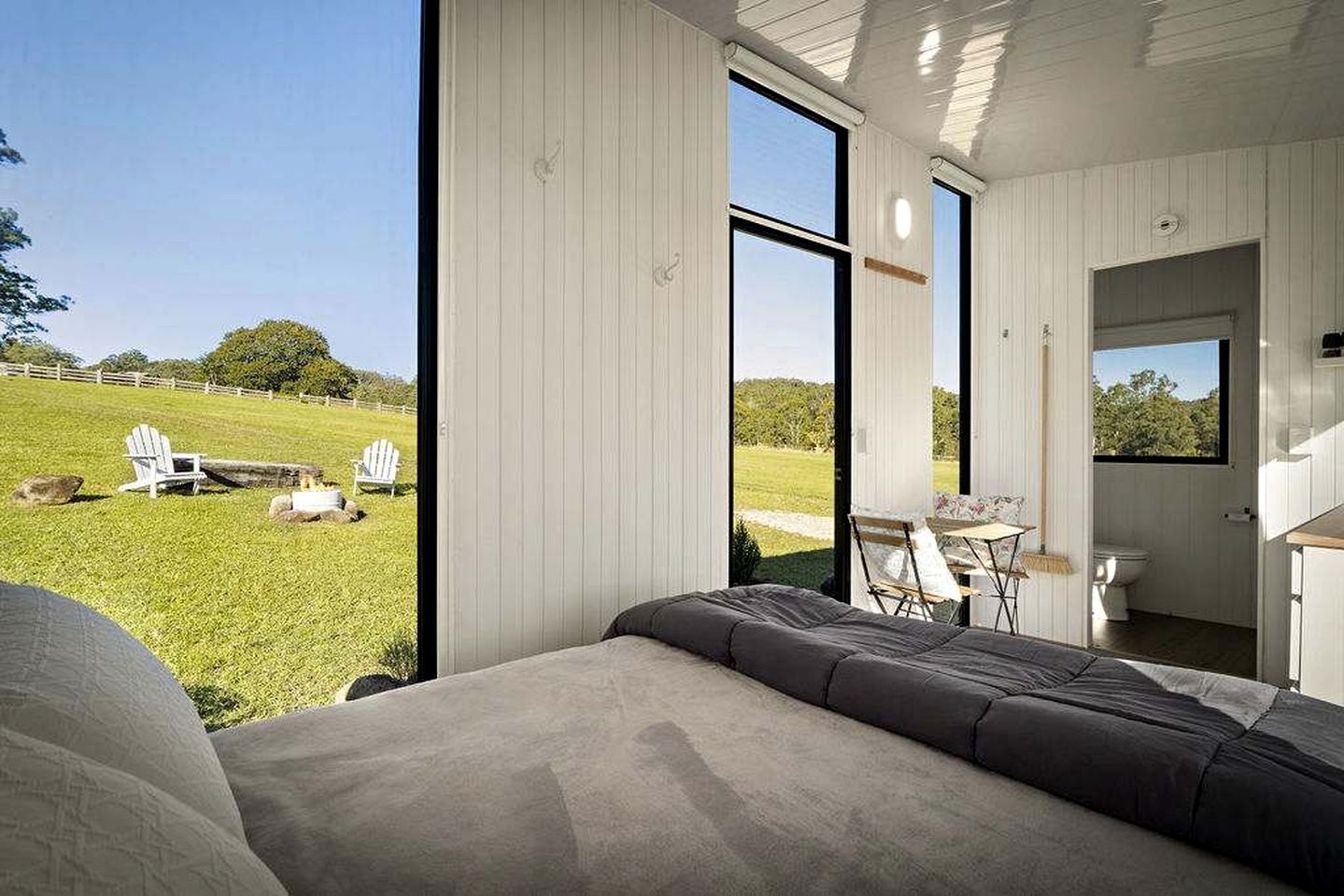 A bedroom with a large window, a bed, and a view of a grassy outdoor area.