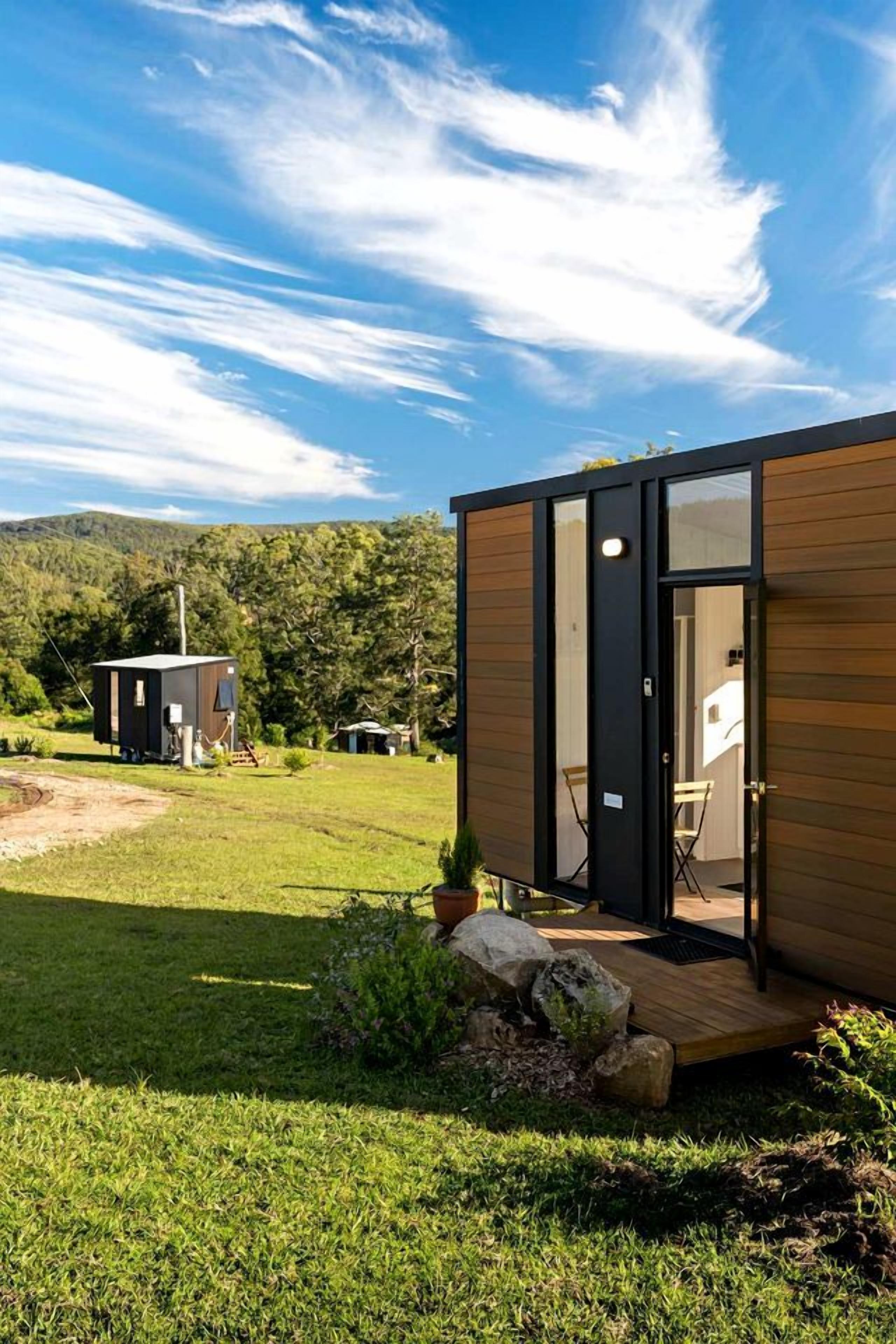 Een modern vakantiehuisje met een houten gevel en een glazen deur, gelegen in een grasrijke omgeving onder een heldere lucht.