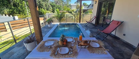 An outdoor dining area with a pool, table set with plates, cutlery, and a pineapple.