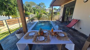 An outdoor dining area with a pool, table set with plates, cutlery, and a pineapple. - Premium 5-bedroom villa · pool · air conditioning · Sud Sauvage (Saint-Philippe)