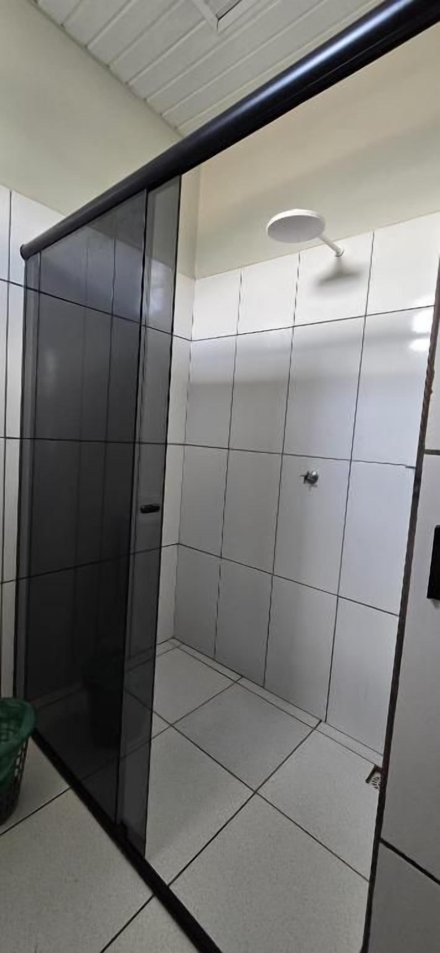 Un baño con cabina de ducha de vidrio, paredes con azulejos blancos y ducha visible.