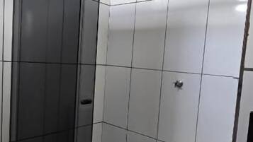 Un baño con cabina de ducha de vidrio, paredes con azulejos blancos y ducha visible.