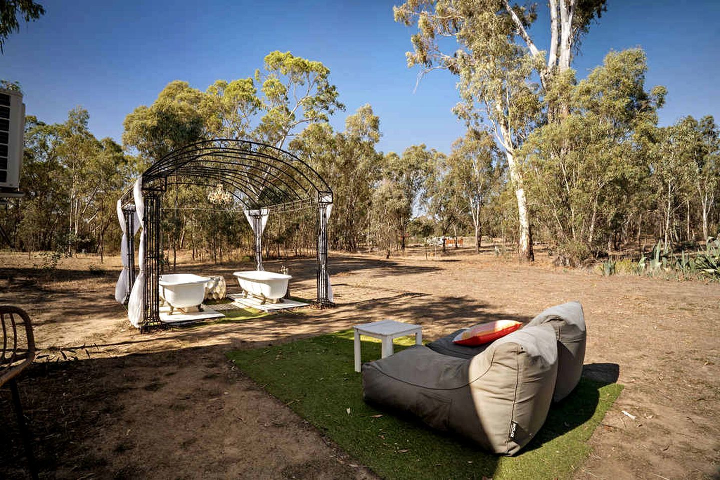 Un'area relax esterna con una pergola in metallo, due vasche da bagno bianche e una panca imbottita.