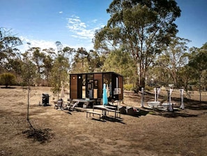 Eine kleine Holzhütte mit einer Terrassenfläche, inklusive Tisch und Stühlen, umgeben von Bäumen.