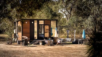 Una cabaña rústica con fachada de madera, un porche con mobiliario exterior y una pequeña zona de piscina.
