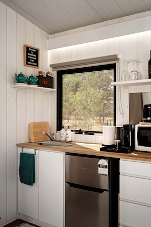 A compact kitchen with a built-in oven, a coffee maker, and a window with a view of trees.