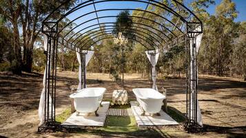 A metal archway with two white bathtubs under it, set in a natural outdoor area with trees.