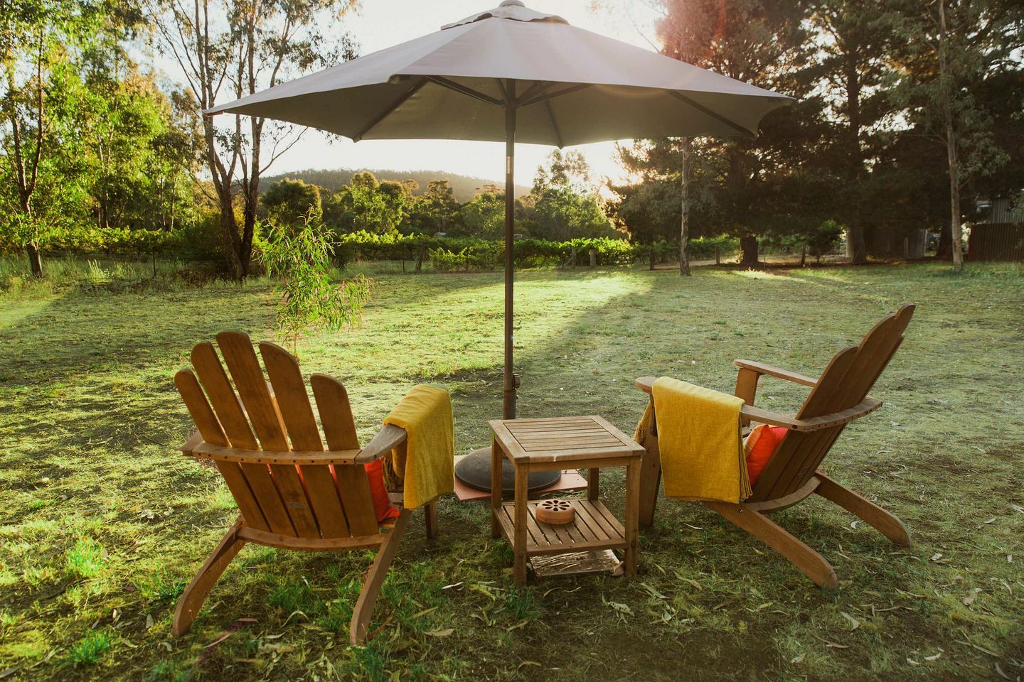 An outdoor seating area with two Adirondack chairs and a small table, under a large umbrella.