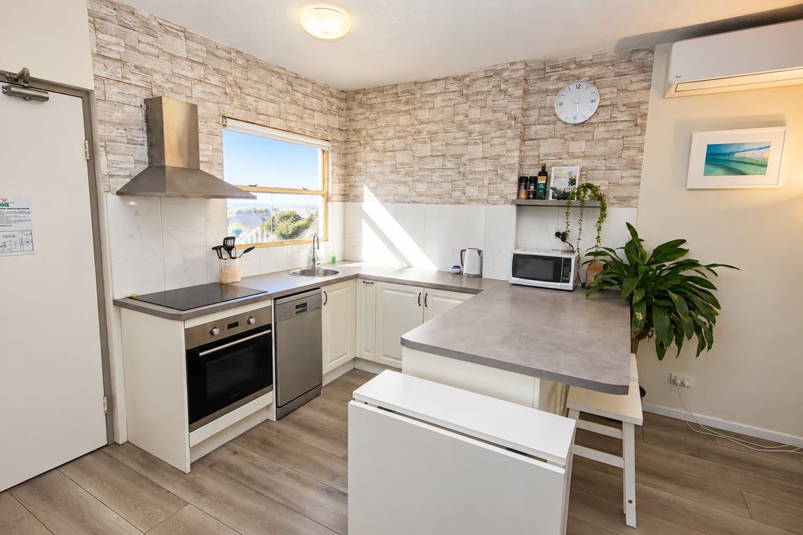 A modern kitchen with a stone backsplash, a built-in oven, a dishwasher, a microwave, and a small island with seating.