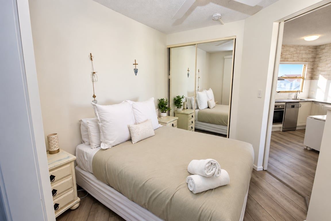 A hotel room with a large bed, bedside tables, a mirror, and a view of the kitchen.