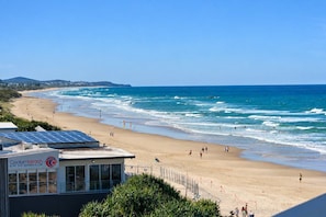 A beach with a surf life saving club building, clear skies, and ocean waves.