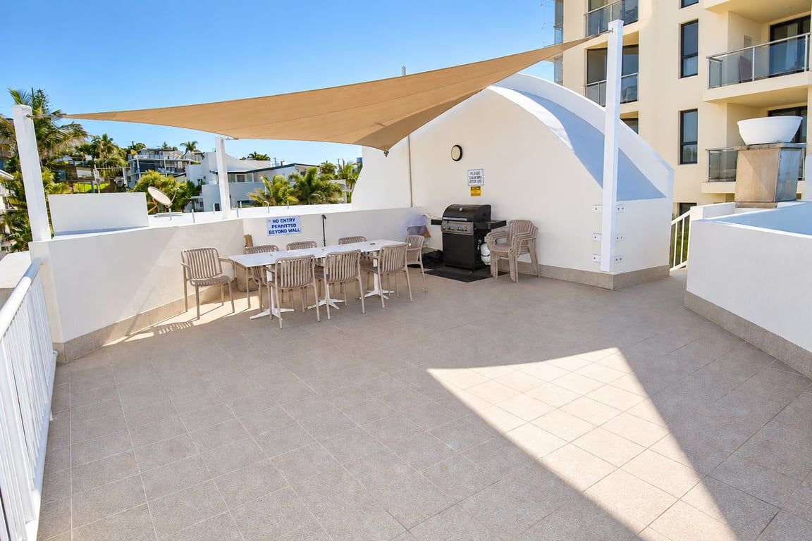 An outdoor patio with a table and chairs, a grill, and a shaded area.