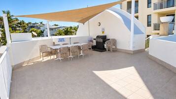 An outdoor patio with a table and chairs, a grill, and a shaded area.