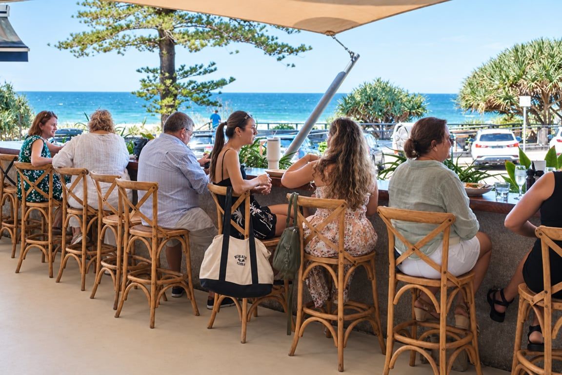 A group of people seated at wicker chairs outdoors with a view of the ocean.