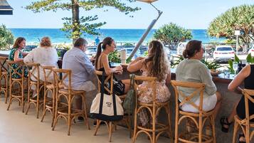 A group of people seated at wicker chairs outdoors with a view of the ocean.