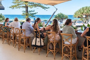 A group of people seated at wicker chairs outdoors with a view of the ocean. - Above the Rest | Coolum Ocean Views & Pool (Sunshine Coast)
