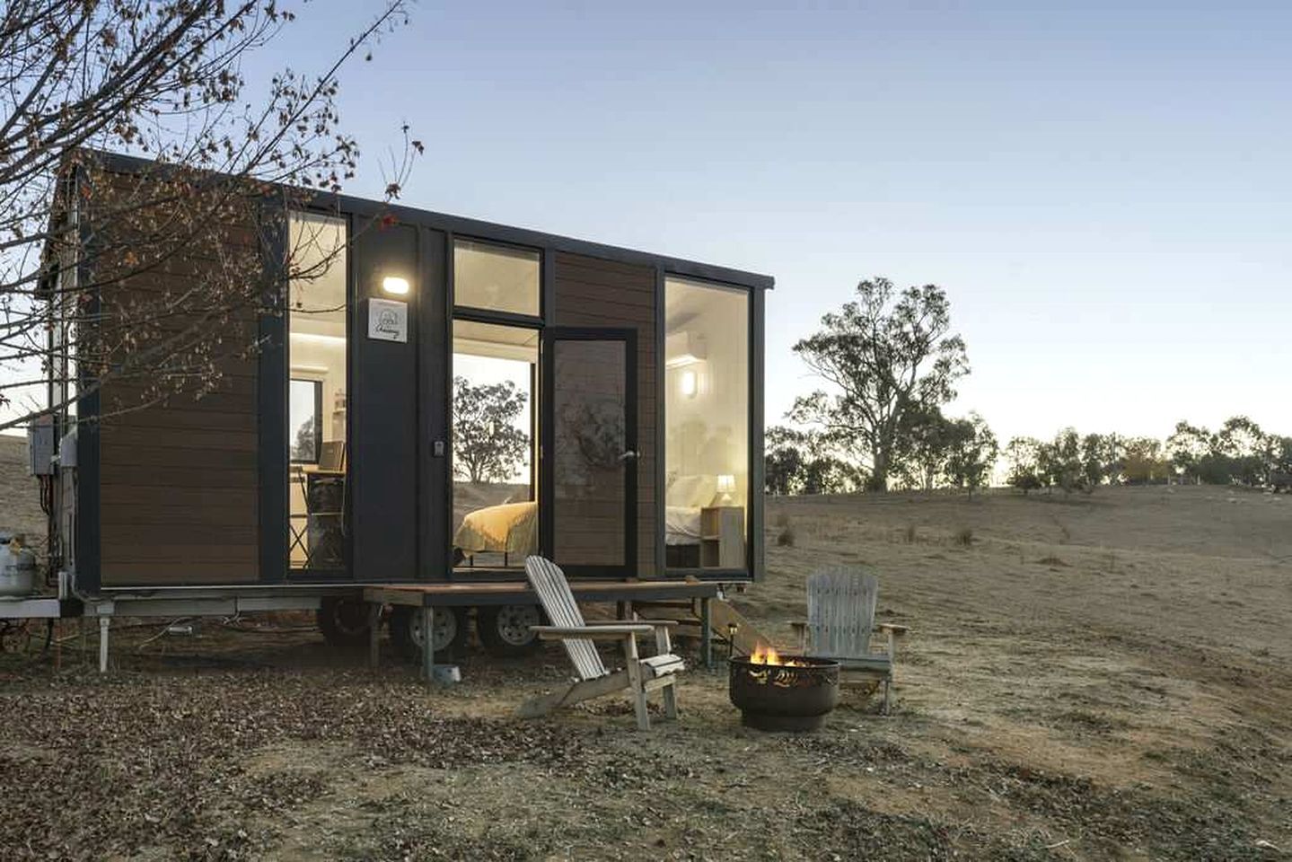 A modern, compact cabin with a large glass door, a small porch, and a fire pit.