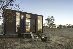 Une cabane moderne et compacte, dotée d’une grande porte vitrée, d’un petit porche et d’un foyer extérieur.