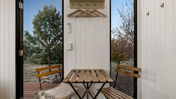 A small outdoor seating area with a wooden table and benches, a hanging coat rack, and a door leading outside.