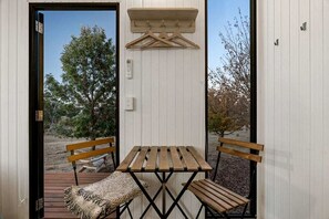 Een klein buitgedeelte met een houten tafel en bankjes, een hangende kapstok, en een deur naar buiten.