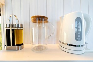 Un thermos en acier inoxydable, une tasse en verre avec un couvercle en liège et une bouilloire électrique blanche, le tout posé sur une surface blanche.