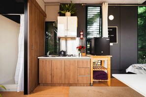 A compact kitchen with a wooden cabinet, a small countertop, a gas stove, and a black refrigerator. - Luxury Tiny Home is Perfect for a Victoria Bush Retreat (Korweinguboora)