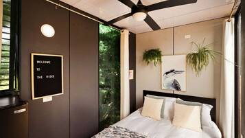 A bedroom with a bed, a ceiling fan, a message board, and a window with a view of trees.