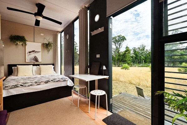 A bedroom with a bed, a desk, and a view of the outdoors.