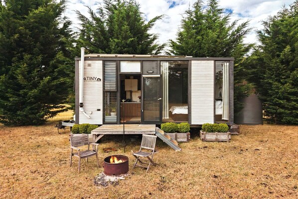 A compact, modern cabin with a glass door entrance, a small deck, and a fire pit.