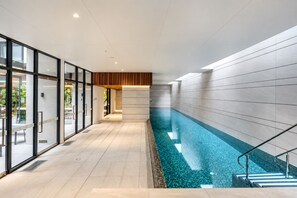 A modern indoor swimming pool with clear water, surrounded by glass walls and a tiled floor. - Mocha Maison | Oversized 2 Bedroom, 2 Bathrooms + 2 Car Parks (Southbank)