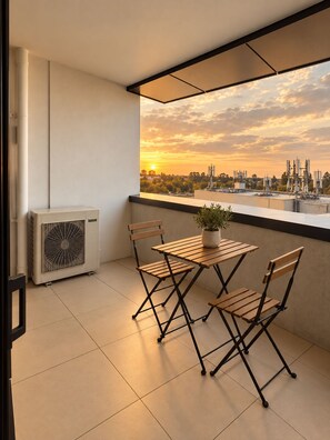 A balcony with a table and chairs, a potted plant, and a view of the sunset over a cityscape. - Mocha Maison | Oversized 2 Bedroom, 2 Bathrooms + 2 Car Parks (Southbank)