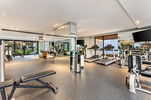 A modern gym with cardio equipment, weight machines, and a mirrored wall. - Mocha Maison | Oversized 2 Bedroom, 2 Bathrooms + 2 Car Parks (Southbank)