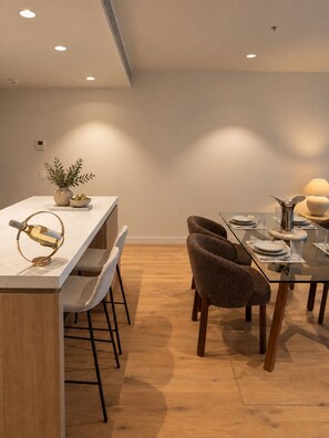 A modern dining area with a long table, chairs, and a decorative wine bottle. - Mocha Maison | Oversized 2 Bedroom, 2 Bathrooms + 2 Car Parks (Southbank)
