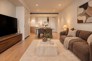 A modern living room with a flat-screen TV, a brown sofa, and a coffee table with decorative items. - Mocha Maison | Oversized 2 Bedroom, 2 Bathrooms + 2 Car Parks (Southbank)