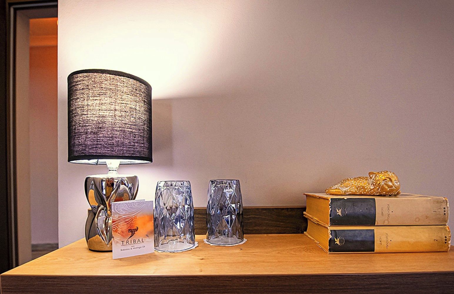Uma mesa com uma lâmpada, três vasos de vidro, um livro e um objeto decorativo.