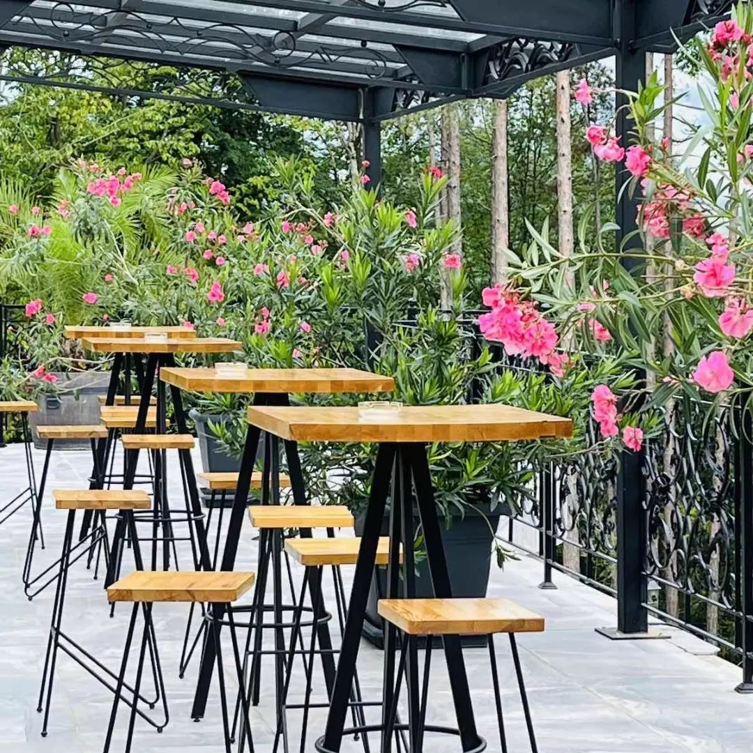 Outdoor seating with tables and chairs, surrounded by lush greenery and flowering plants.