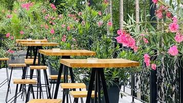 Outdoor seating with tables and chairs, surrounded by lush greenery and flowering plants.