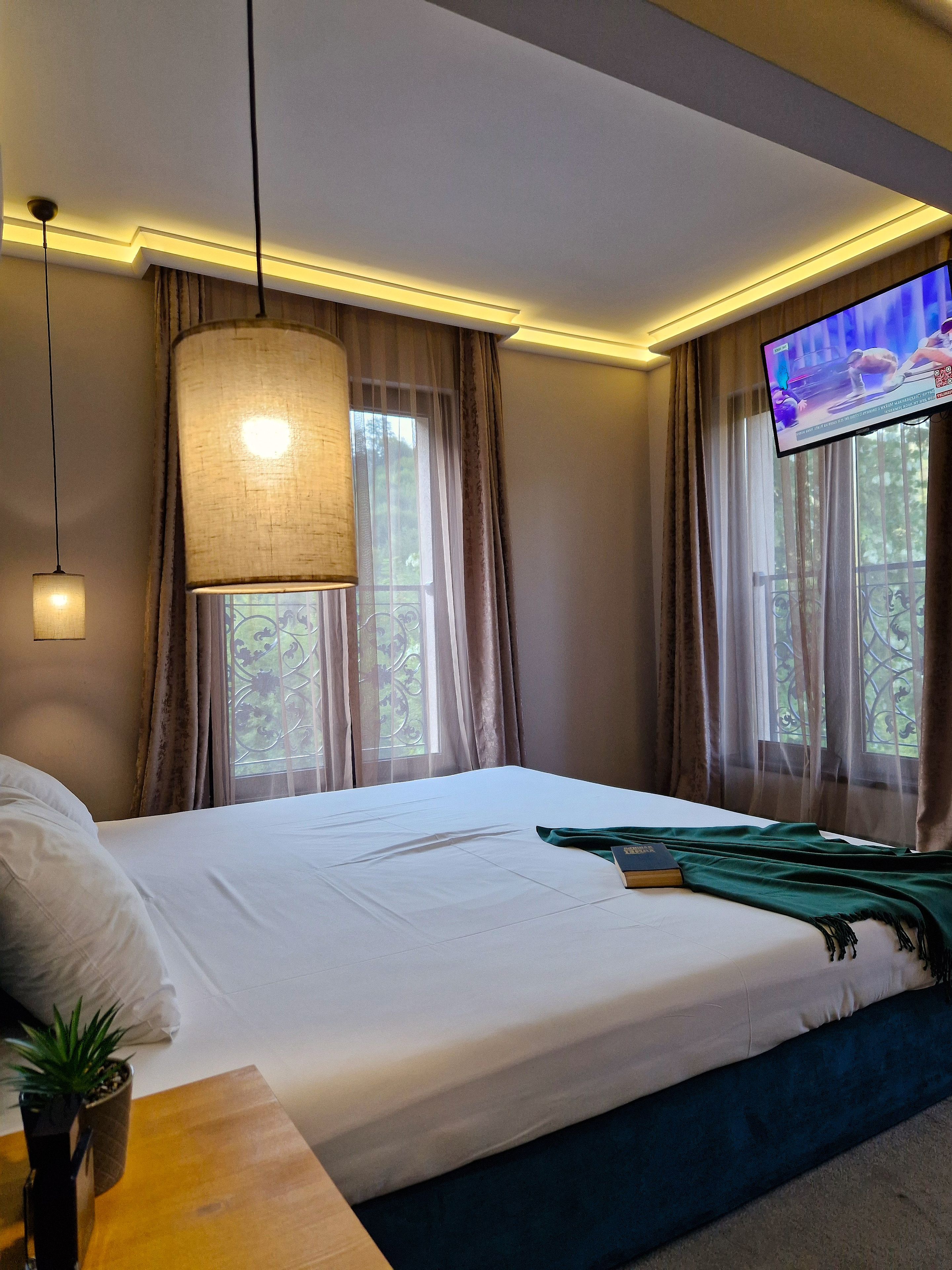 Una habitación de hotel con una cama, televisión, ventana con cortinas y una lámpara.