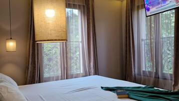 Una habitación de hotel con una cama, televisión, ventana con cortinas y una lámpara.