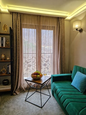 A living room with a green sofa, a small table with a fruit bowl and a glass, and a bookshelf with books and decorative items.