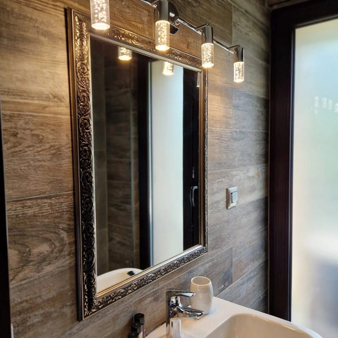 A bathroom with a large mirror, a white sink, and a cup.