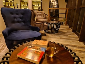 Une pièce comprenant un fauteuil bleu, un fauteuil beige, une table ronde en bois avec un livre et une tasse en verre, ainsi qu’une petite table ronde sur laquelle est posée une plante.