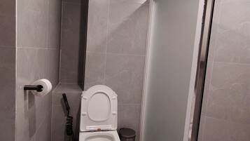 Casa de banho moderna com sanita, secador de mãos e um contentor de lixo.
