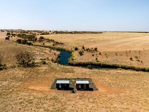 A rural landscape with two cabins near a river.