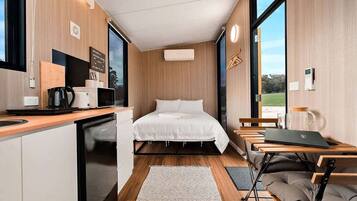 A compact room with a bed, a small kitchenette, and a seating area with a laptop.